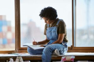 בחורה צעירה יושבת עם מחברת ציור