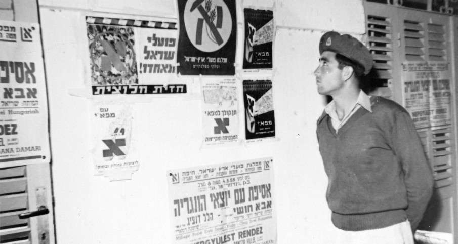 חייל מביט על מודעות קיר הקוראות להצביע למפאי בבחירות 1955 (מתוך ארכיון על שם אבא חושי (חיפה) )