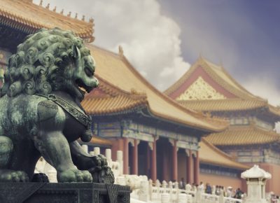 Old imperial lion sculpture in front of historical Forbidden City buildings.